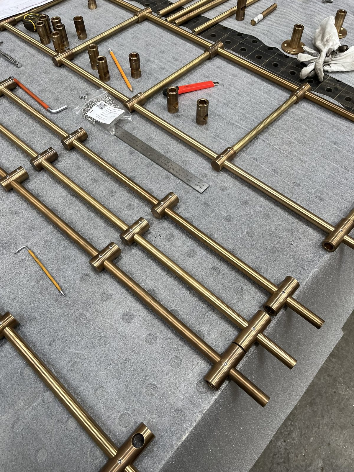 A batch of brass shelving frames laid out on the bench
