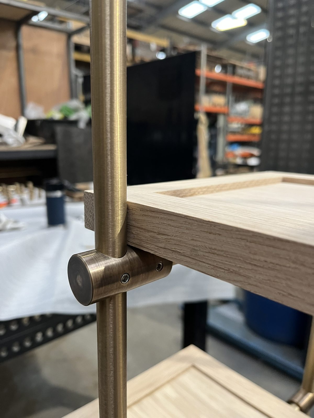 A brass upright and connector holding an oak shelf, close up