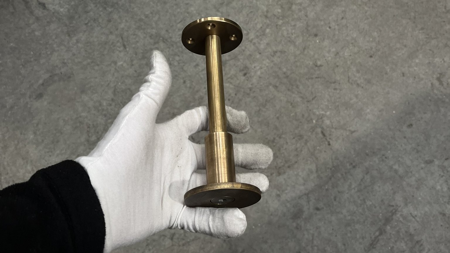 A finished brass shelving upright and base plate held in a white cotton glove