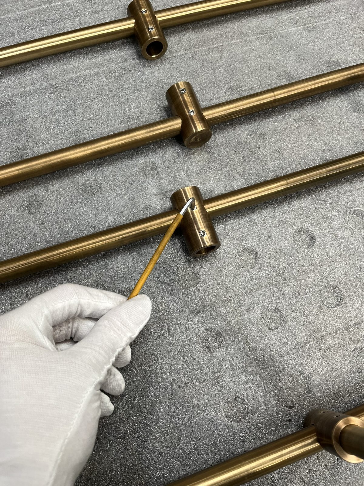 A gloved hand fitting brass connectors onto shelf rails with a hex key